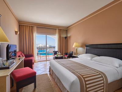 Hotelzimmer mit Doppelbett, Sitzbereich und Meerblick durch großen Balkonfenster.