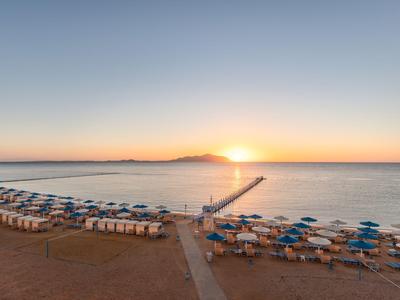 Sonnenuntergang am Strand mit blauen Sonnenschirmen und einem Steg, der ins Meer führt.