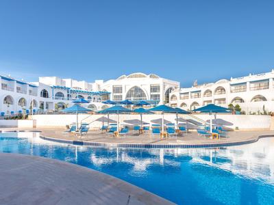 Moderner Hotelkomplex mit Pool, blauen Sonnenschirmen und klarem Himmel.