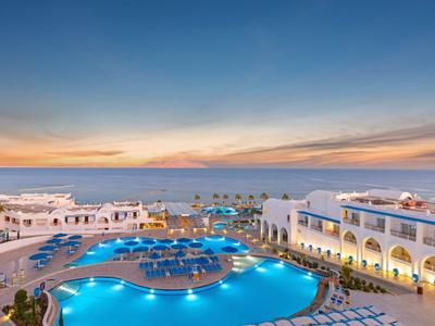 Luxuriöse Hotelanlage mit beleuchtetem Pool und Blick auf das Meer bei Sonnenuntergang.