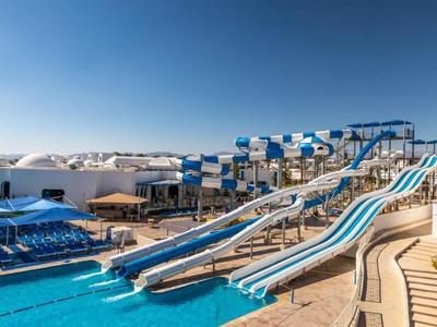 Wasserpark mit großen, gewundenen Wasserrutschen und einem Pool unter blauem Himmel.
