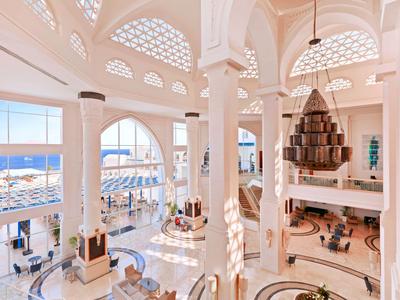 Helles, großes Hotellobby mit hohen Bögen, weißen Säulen und Blick auf das Meer.
