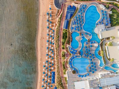 Luftaufnahme eines Hotelpools mit mehreren Swimmingpools und Sonnenschirmen am Strand.