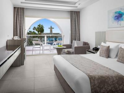 Modernes Hotelzimmer mit Doppelbett, Sitzbereich und Blick auf Terrasse und Pool durch einen Bogen.