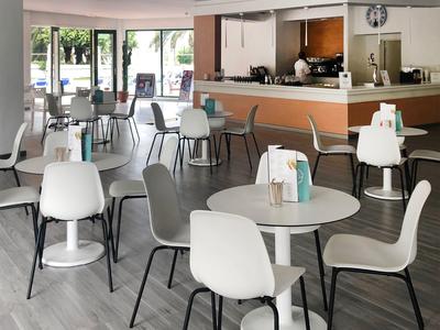 Moderne Hotellounge mit weißen und grauen Stühlen, runden Tischen und einer Bar im Hintergrund.