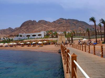 Vista di una passeggiata lungo una spiaggia con hotel e montagne sullo sfondo.