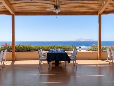 Ristorante all'aperto con tavoli e sedie, vista sul mare blu e cielo sereno.