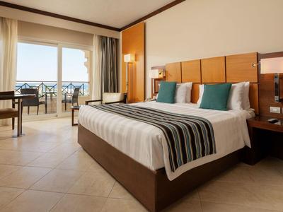 Camera d'hotel moderna con letto grande, balcone e vista mare alla luce del giorno.