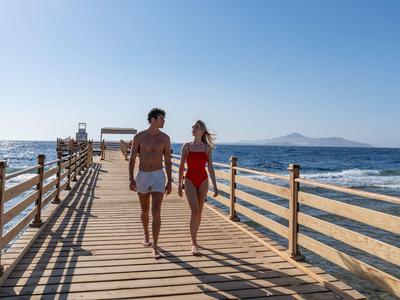 Una coppia cammina su un pontile di legno vicino al mare sotto un cielo sereno.
