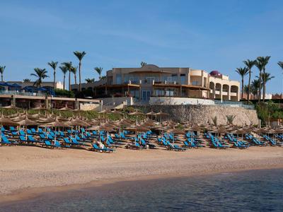 Hotel con lettini sulla spiaggia di sabbia e palme sotto un cielo blu limpido.