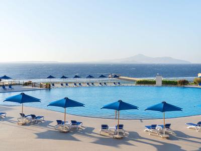 Grande piscina all'aperto con ombrelloni blu e vista sul mare sullo sfondo