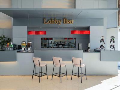 Bar della hall moderna con tre sgabelli, lampade rosse e bancone grigio minimalista.