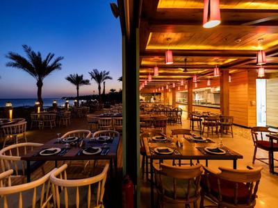Abendliche Terrasse und Innenbereich eines Restaurants mit Blick auf Palmen und Meer bei Sonnenuntergang.