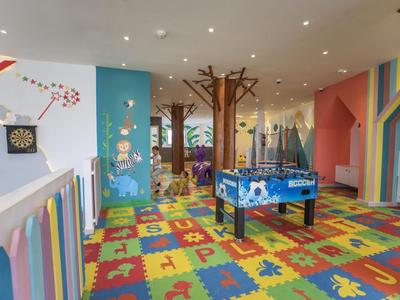 Bunter Kinderspielraum mit Spielautomat, Dartboard und dekorativen Baumstrukturen in einem Hotel.