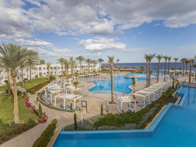 Hotelpool mit Liegestühlen und Palmen unter bewölktem Himmel am Meer.
