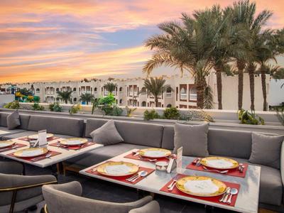 Terrasse mit gedeckten Tischen und Palmen bei Sonnenuntergang in einem Hotel.