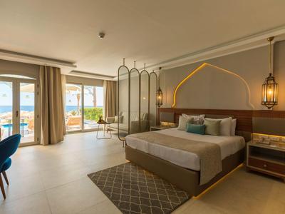 Helles Hotelzimmer mit großem Bett, Sitzbereich und Meerblick durch bodentiefe Fenster.