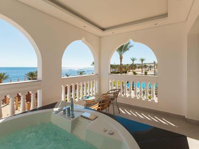 Balkon mit Whirlpool und Blick auf Pool, Palmen und Meer an einem sonnigen Tag.