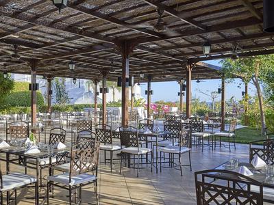 Überdachte Terrasse mit dekorativen Stühlen und Tischen in einem Hotel mit Blick auf das Meer.