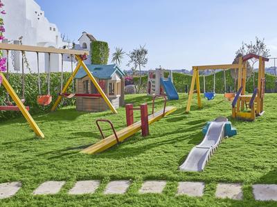 Kinderspielplatz mit Schaukeln, Rutschen und Wippen auf gepflegtem Rasen bei gutem Wetter.