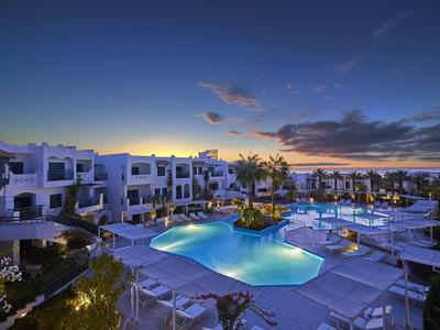Luxushotel mit beleuchtetem Pool, Palmen und Sonnenterrasse bei Sonnenuntergang.