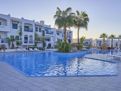 Moderner Hotelpool mit Liegestühlen und Palmen in einer ruhigen Urlaubsanlage.
