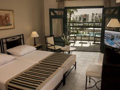 Modern eingerichtetes Hotelzimmer mit Doppelbett, Balkon und Blick auf einen Pool.