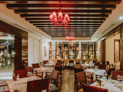 Ristorante elegante con soffitto a travi di legno, lampadari rossi e tavoli apparecchiati.