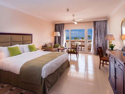 Camera d'hotel luminosa con letto grande, area salotto e balcone con vista sul mare.