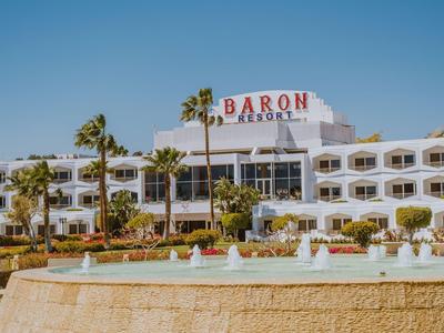 Hotel bianco con scritte rosse e fontana in primo piano sotto un cielo sereno.