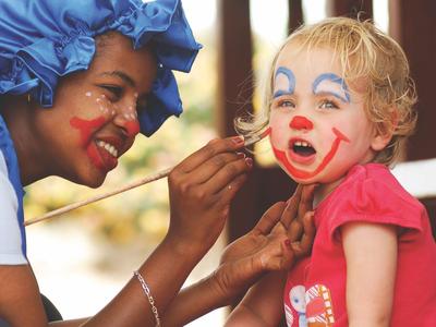 Una donna dipinge un volto da pagliaccio colorato sul viso di una bambina.