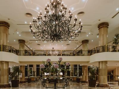 Elegante hall dell'hotel con lampadari, grandi colonne e composizione floreale al centro.