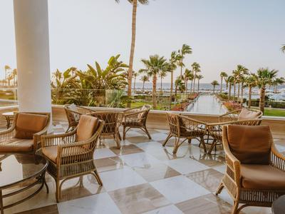 Terrazza con sedie in rattan e tavoli con vista sulle palme e sul mare.