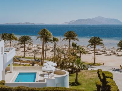 Hotel con piscina, palme e vista sulla spiaggia e sul mare sotto un cielo limpido.