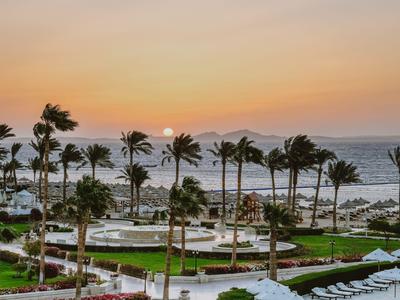 Tramonto su un giardino dell'hotel con palme e vista su mare e montagne.