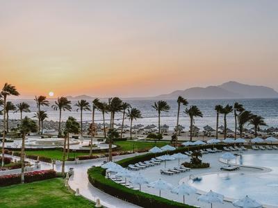 Tramonto su una piscina d'hotel con palme e vista sul mare e le montagne.