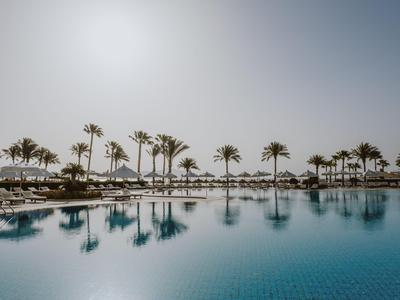 Grande piscina con palme e lettini sotto un cielo sereno in un resort.