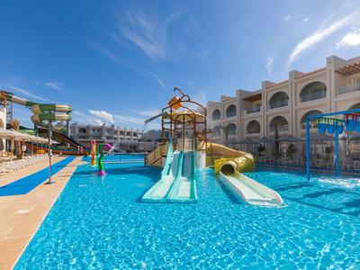 Ein Pool mit Rutschen und Wasserspielplatz vor einem Hotelgebäude unter blauem Himmel.