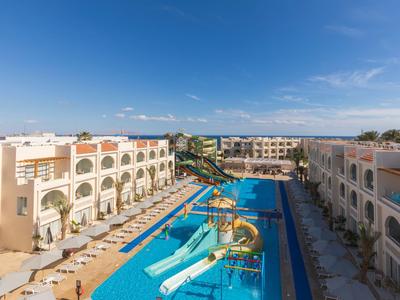 Großer Hotelpool mit Wasserrutschen, umgeben von weißen Gebäuden und Sonnenschirmen unter blauem Himmel.