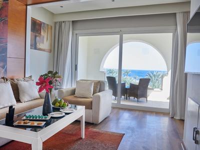 Helle Hotel-Lounge mit Sofa, Sesseln, Blumen und Blick auf Terrasse mit Meerblick.