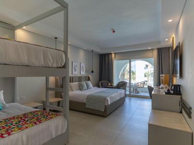 Modernes Hotelzimmer mit Etagenbett, Doppelbett und Balkon mit Blick auf ruhige Landschaft.