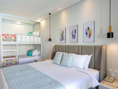 Helles Hotelzimmer mit Doppelbett, Etagenbett und moderner Wanddekoration.