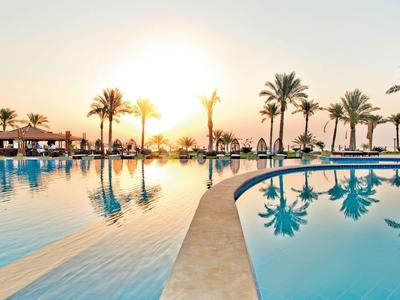 Großer Außenpool mit Palmenspiegelung bei Sonnenuntergang in einem Resort.