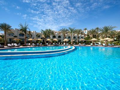 Großer Hotelpool mit klarem blauem Wasser und Palmen unter strahlend blauem Himmel.