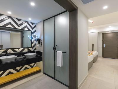 Modernes Hotelzimmer mit Waschbeckenbereich, Dusche und einem Bett im Hintergrund.