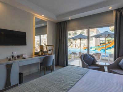 Modernes Hotelzimmer mit Bett, Sitzbereich und Blick auf den Pool mit Sonnenschirmen.