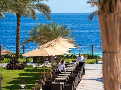 Hotelterrasse mit Sitzbereichen, Sonnenschirmen und Blick auf das blaue Meer bei klarem Himmel.