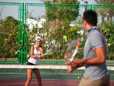 Ein Paar spielt Tennis auf einem Außenplatz eines Hotels bei sonnigem Wetter.