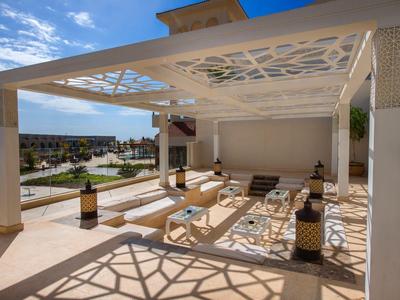 Moderner Außenbereich mit Pergola, Sonnenliegen und ornamentalem Schattenmuster bei Sonnenschein.