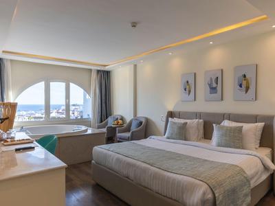 Modernes Hotelzimmer mit großem Bett, Sitzbereich, Schreibtisch und Blick auf das Meer.